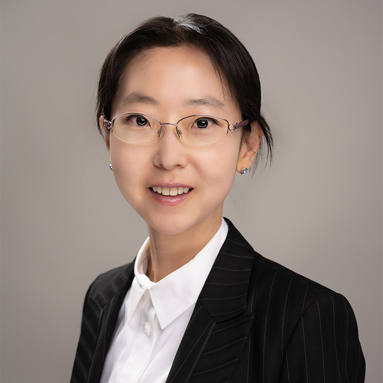 Professional headshot of a woman wearing a black blazer, white button-up shirt and glasses.